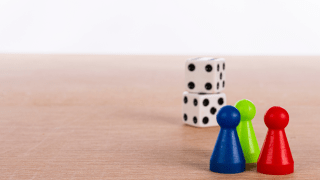 drei Spielfiguren (blau, grün, rot) am rechten Bildrand, im Hintergrund zwei Würfel
