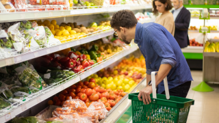 Ein Mann steht gebückt vor dem Gemüseregal und schaut in die Auslage.