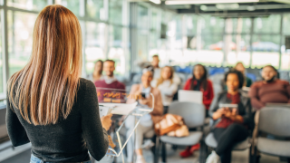 Eine Studentin hält einen Vortrag vor einer Gruppe Studierender.