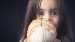 Ein verängstigtes Kind hält ein Kuscheltier vor das Gesicht.