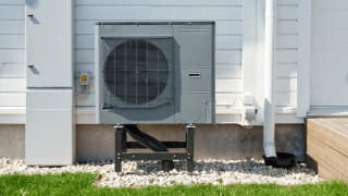 Eine an einer Hauswand angebrachte Wärmepumpe, die von der Sonne angestrahlt wird.