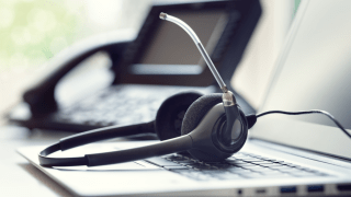 Ein Headset liegt auf einem Laptop, im Hintergrund steht ein Telefon