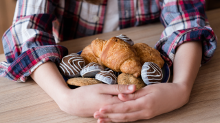 Ein Kind legt die Arme um vor sich auf dem Tisch liegendes Gebäck.
