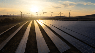 Die Sonne geht auf über eine Feld aus Photovoltaik-Anlagen und Windräder.