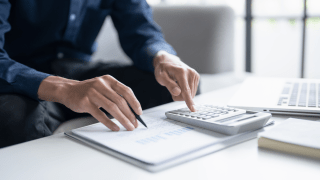 eine Person sitzt am Tisch vor Rechnungen und prüft diese mit einem Taschenrechner.