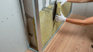 Ein Handwerker dämmt eine Wand mit Mineralwolle.