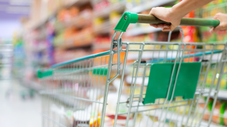 Ein Einkaufswagen wird vor einem Regal durch den Supermarkt geschoben