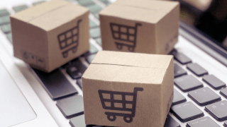 kleine Pakete mit einem Einkaufswagensymbol liegen auf einer Laptop-Tastatur.