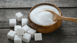 Auf einem Tisch sind Zuckerwürfel neben einer Schale mit Zucker gestapelt.