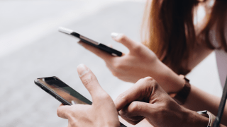 Jugendliche sitzen nebeneinander mit Smartphones in den Händen.