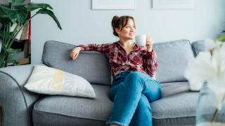 Eine Frau sitz entspannt mit einer Tasse in der Hand auf dem Sofa